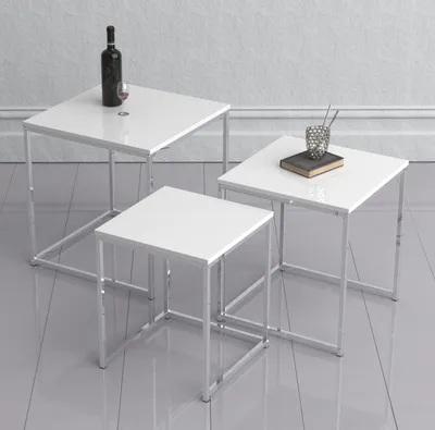Three nesting tables with white tops and silver metal frames are arranged on a light gray floor against a white wall.