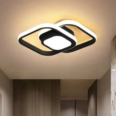 A modern ceiling light fixture with a black and white design, installed on a ceiling above a hallway with wooden doors.