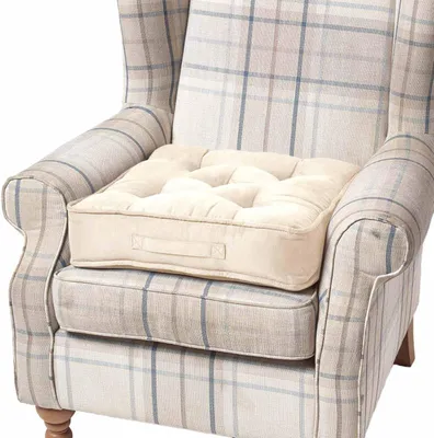 A cream-colored seat cushion is placed on a plaid armchair.