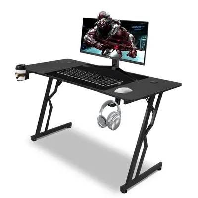 A black Z-shaped gaming desk with a monitor, keyboard, mouse, cup holder, and headphones.