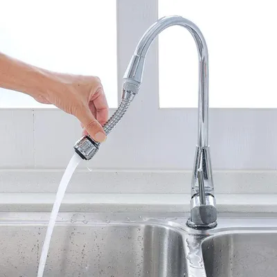 A hand is holding a flexible faucet extension over a sink, with water flowing through it.