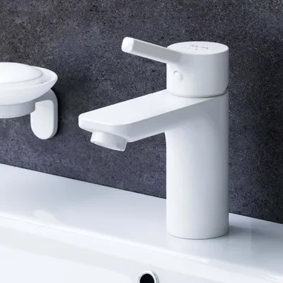 A white bathroom faucet and soap dish are shown against a dark gray tiled wall and a white countertop.