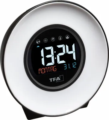 A digital alarm clock with a circular display showing the time, date, and day of the week. It has a white illuminated outer ring and a black inner frame.