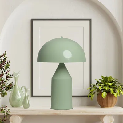 A green mushroom-shaped table lamp is displayed on a shelf with decorative vases and a potted plant.