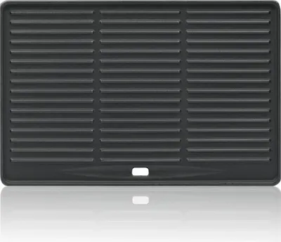 A top-down view of a black cast iron grill plate with horizontal ridges, placed on a reflective surface.