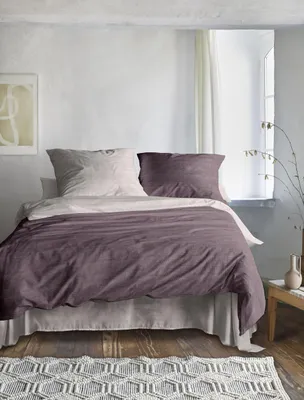 A bedroom scene with a bed made with the featured duvet cover and pillows, set against a textured wall and a window.