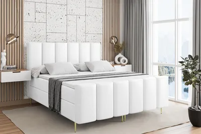 A white upholstered bed with gold legs in a bedroom setting.