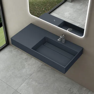 A modern bathroom sink with a faucet, mounted on a wall above a tiled floor, with a large mirror reflecting an outdoor scene.