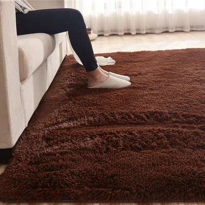 A person's legs and feet are visible, resting on a plush brown rug next to a cream-colored sofa. The scene suggests a comfortable, domestic setting.
