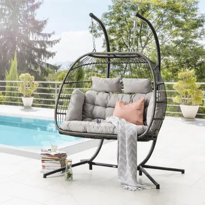 A hanging egg chair with cushions is placed on a patio next to a swimming pool.