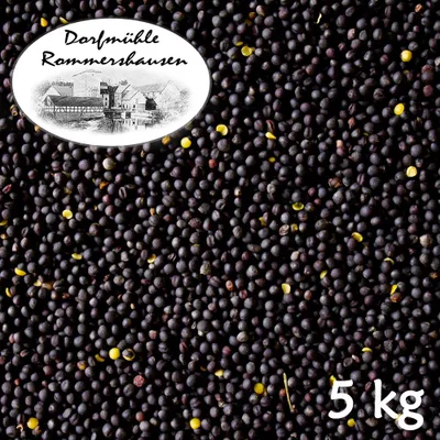 A pile of dark seeds, likely rapeseed or mustard seeds, with a white oval label in the upper left corner featuring a drawing of buildings and text, and the number '5 kg' in the bottom right corner.