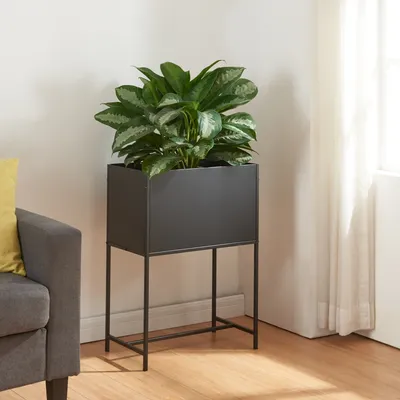 A plant stand with a plant on it, next to a sofa and a curtain.