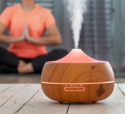 A person is meditating in the background while an essential oil diffuser is in the foreground.