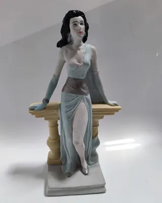 Frau im hellblauen Kleid, das an einen griechischen Chiton erinnert. Sie lehnt an einer Balustrade.