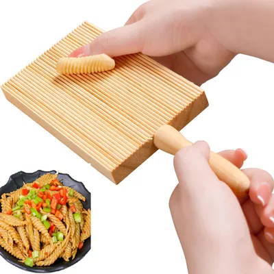 Hands using a wooden pasta maker to create ridged pasta shapes, with a plate of finished pasta in the foreground.