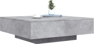 A modern, square coffee table with a concrete-like finish, featuring a small potted plant and a coffee cup on top.