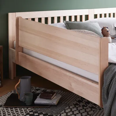 Close-up side view of a wooden bed frame with bedding and pillows.