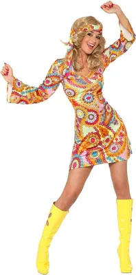 A woman wearing a 70s-style hippie costume, including a colorful patterned dress and yellow boots, posing against a white background.