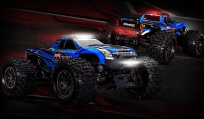 Two blue remote-controlled monster trucks are shown in a dynamic, dark setting with red accents.
