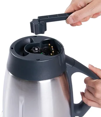 A close-up shot of a person's hands using a tool to interact with the top of a kitchen appliance.