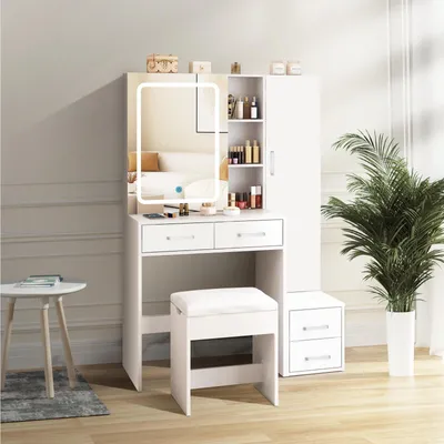 A white vanity set with a lighted mirror, drawers, and a stool, placed in a room with a plant and a small table.