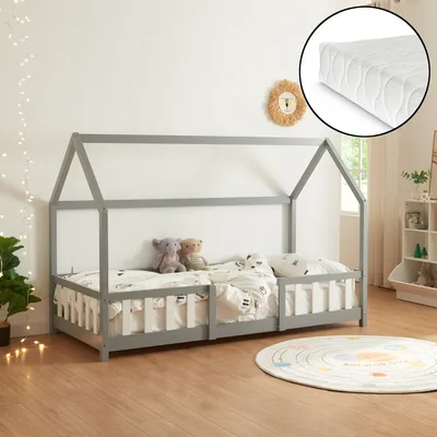 A child's house-shaped bed with bedding and stuffed animals, set in a room with decorative lights and a rug.