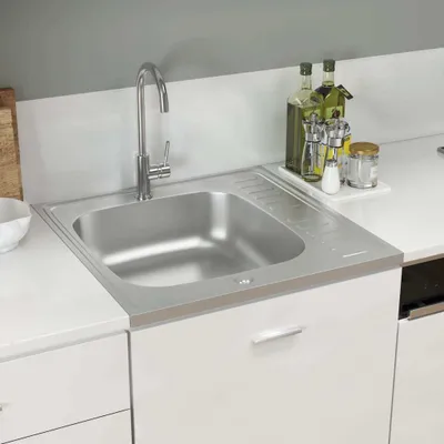 A stainless steel kitchen sink with a faucet and a draining board, set into a white countertop.