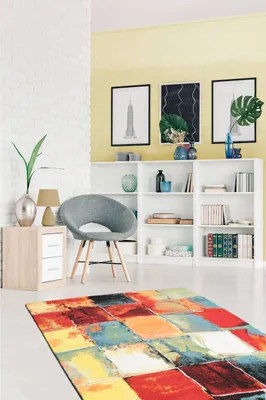A living room scene with a colorful rug in the foreground, a chair, and bookshelves in the background.