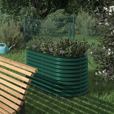 A green raised garden bed filled with herbs sits in a garden next to a wooden bench.