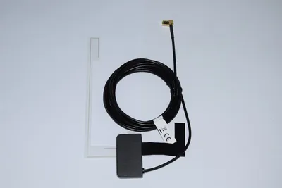 A black antenna cable is coiled on a white background, next to a clear plastic antenna element. A black rectangular module is attached to the cable.