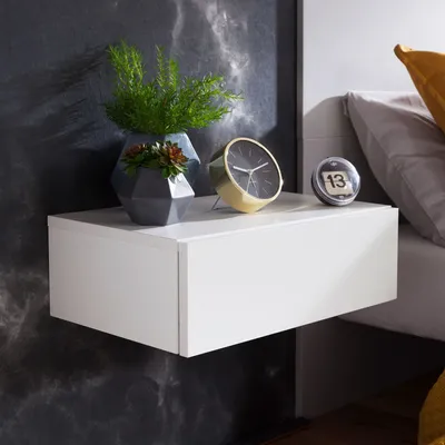A white floating nightstand with decorative items on top, next to a bed.