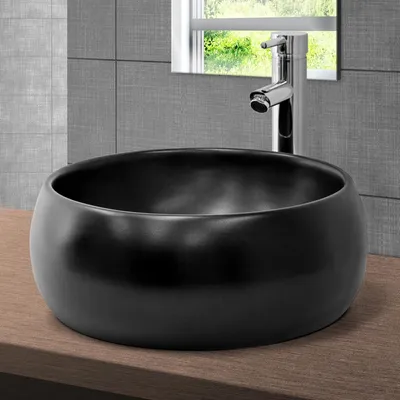 A black ceramic vessel sink sits on a wooden countertop, with a modern chrome faucet behind it and a tiled wall in the background.