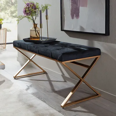 A black velvet bench with a gold metal frame is placed in a room with a painting on the wall and a vase with flowers on it.