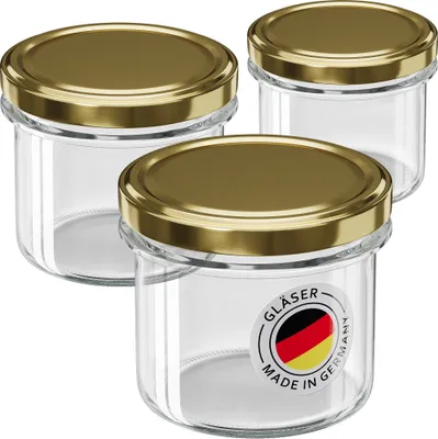 Three glass jars with gold screw-on lids are arranged in a group against a white background. One jar in the foreground has a circular label with the German flag and text.