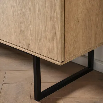A close-up shot of the bottom corner of a wooden sideboard with a black metal leg.