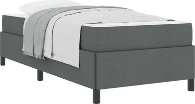 A dark gray boxspring bed with a white mattress, white sheets, and a gray blanket.