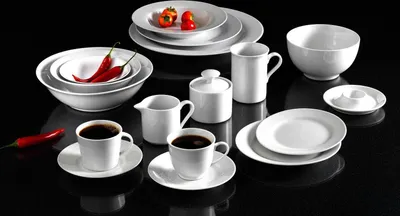 A collection of white porcelain dishes and cups arranged on a black surface.