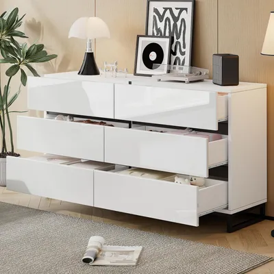 A white, high-gloss sideboard with six drawers is shown in a well-lit room with a plant and decorative items on top.