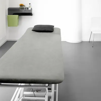A clean and sterile-looking room with a treatment table, a shelf with items, and a chair in the background.