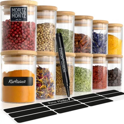 A collection of glass spice jars with bamboo lids, filled with various spices and herbs. A marker is shown writing on a label.