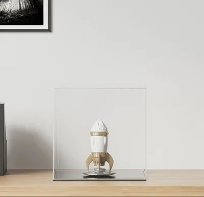 A rocket-shaped object displayed inside a clear acrylic cube on a wooden surface.