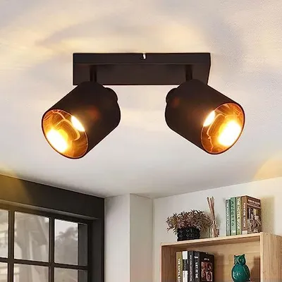 A black ceiling light fixture with two adjustable spotlights, each with a gold interior, mounted on a white ceiling.