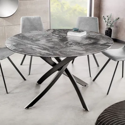 A round dining table with a marble-like top and a black metal base, surrounded by chairs in a dining room setting.