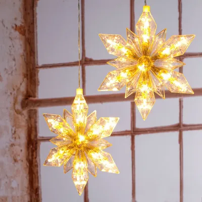 Two illuminated star-shaped decorations hang in front of a window.