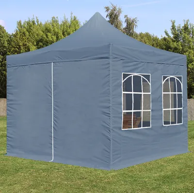 A gray pop-up tent with windows is set up on a grassy lawn with trees in the background.