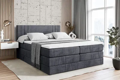 A bedroom scene featuring a large box spring bed with bedding, a nightstand, and decorative elements.