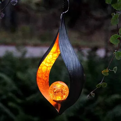 A decorative solar lantern hanging from a tree branch in a garden at dusk.