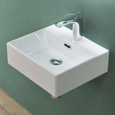 A white ceramic sink with a chrome faucet is mounted on a green wall, with a wooden surface visible at the bottom.