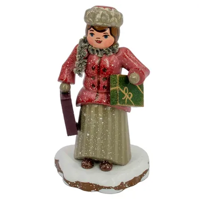 Ein fröhliches Winterkind in rotem Mantel und Mütze hält ein Geschenk und eine Tasche in den Händen während es auf einem schneebedeckten Sockel steht und die Vorfreude auf Weihnachten spürbar wird