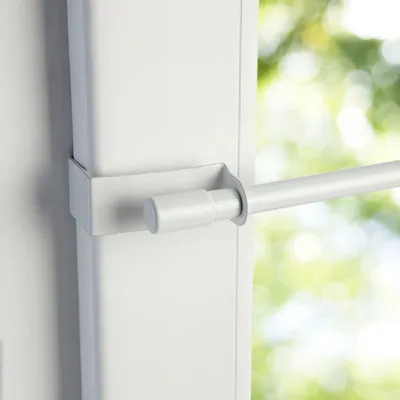 A close-up view of a white tension rod mounted on a white frame, with a blurred green and white background suggesting an outdoor environment.